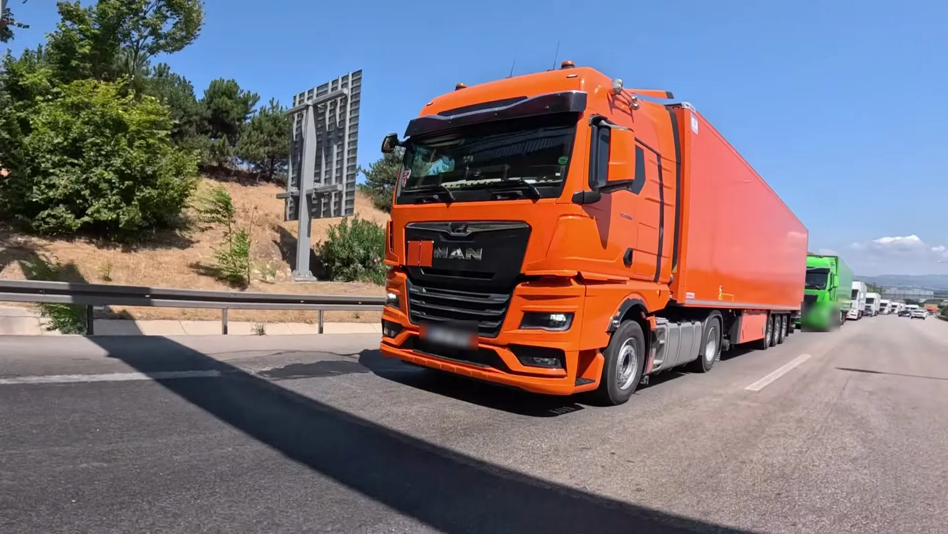 Otoyolda turuncu MAN TGX çekici ve arkasında konvoy