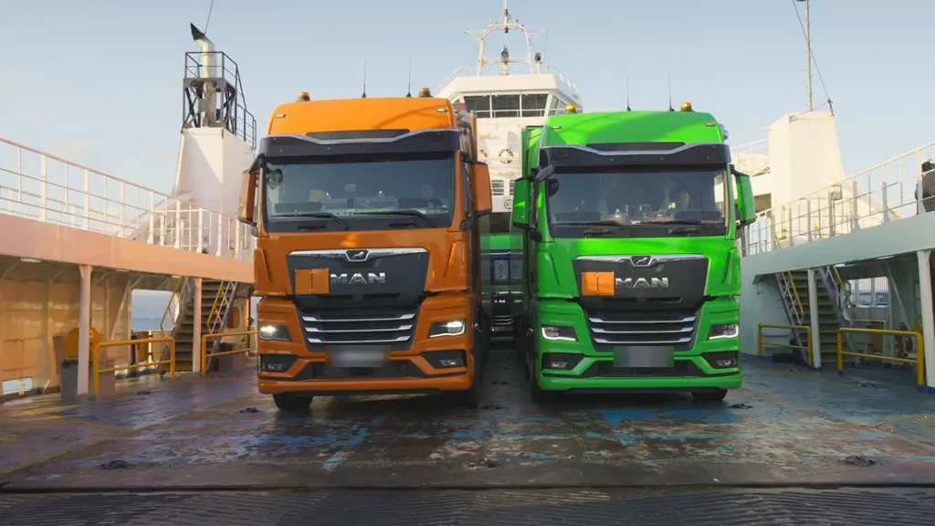 Feribotta yan yana turuncu ve yeşil MAN TGX çekiciler